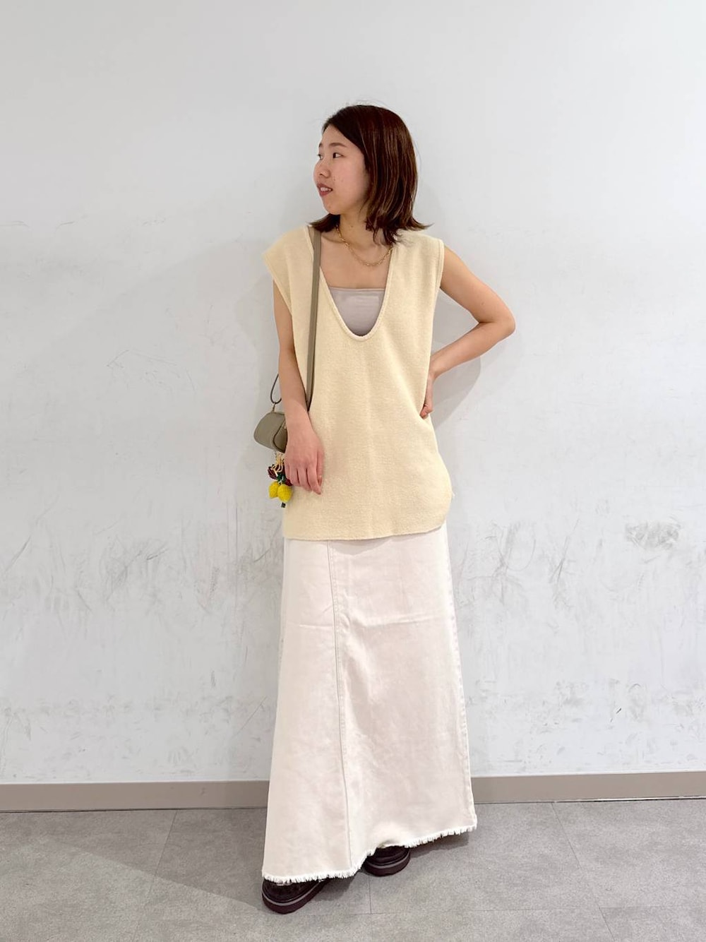 オレンジ系のキャミソール、ホワイト系のスカート、ベージュ系のベストを着用したレディースの夏コーディネートの1枚目の写真