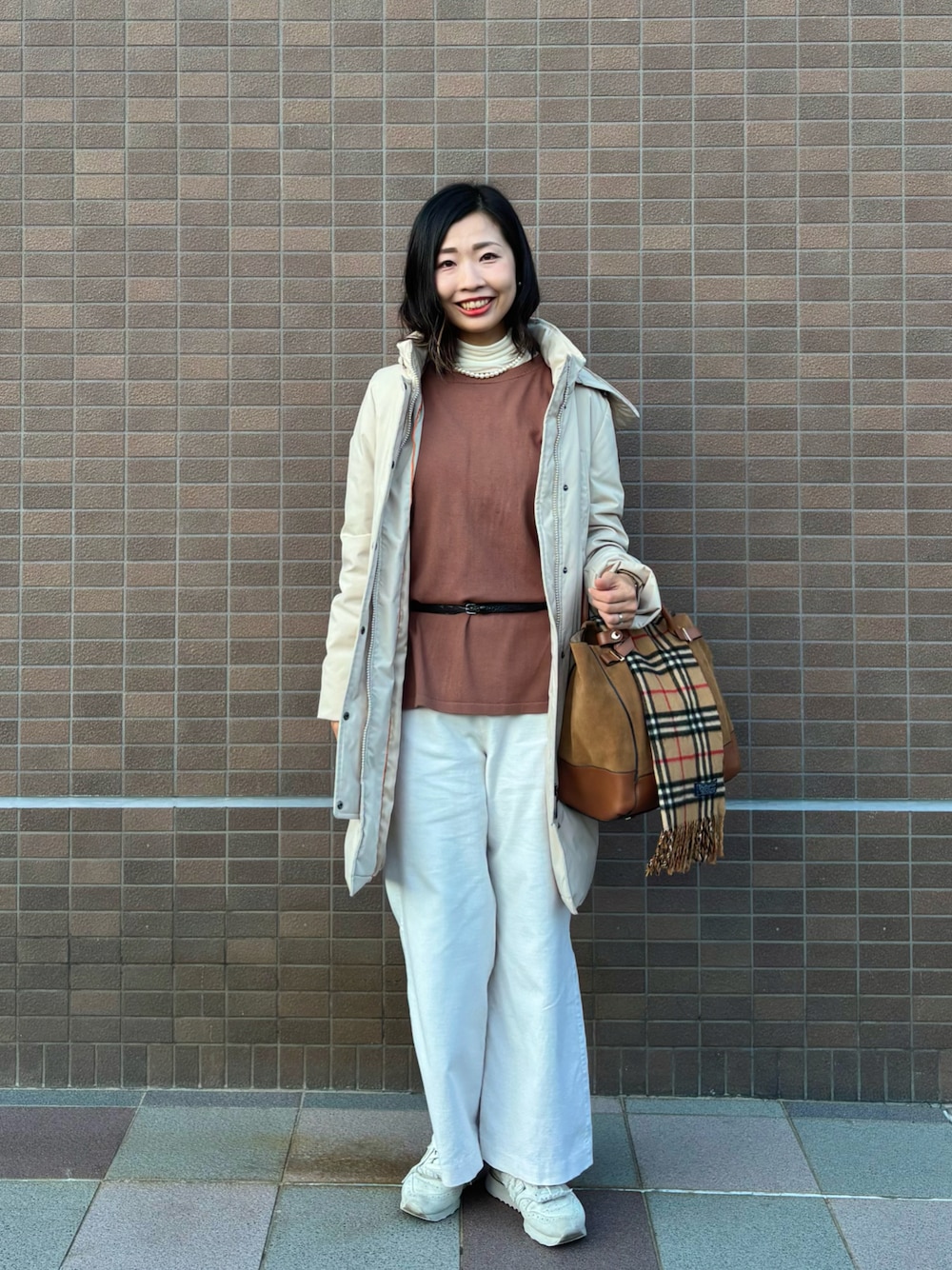 ブラウン系のニット/セーター、ホワイト系のTシャツ/カットソー、ベージュ系のダウンジャケット/コートを着用したレディースの秋コーディネートの1枚目の写真