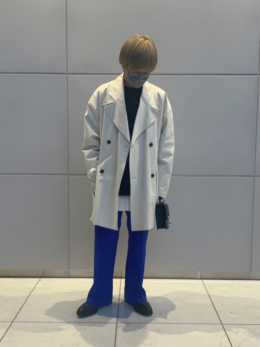 ベージュ系のステンカラーコート、ブラック系のショルダーバッグ、ブラック系のブーツを着用したメンズの春コーディネートの1枚目の写真