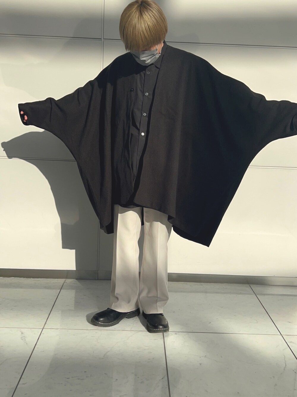 ブラック系のポンチョ、ブラック系のドレスシューズ、ホワイト系のパンツを着用したメンズの春コーディネートの1枚目の写真