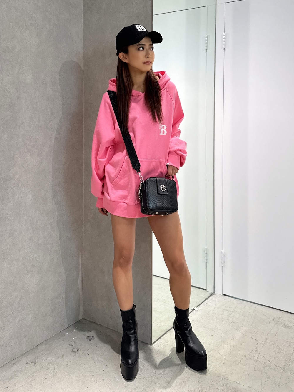 ピンク系のパーカー、ブラック系のショルダーバッグ、ブラック系のブーツを着用したレディースの冬コーディネートの1枚目の写真