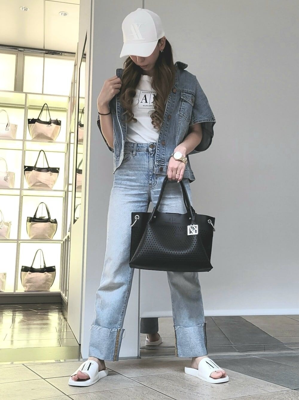 ブラック系のハンドバッグ、ホワイト系のサンダル、ブルー系のデニムジャケットを着用したレディースの夏コーディネートの1枚目の写真