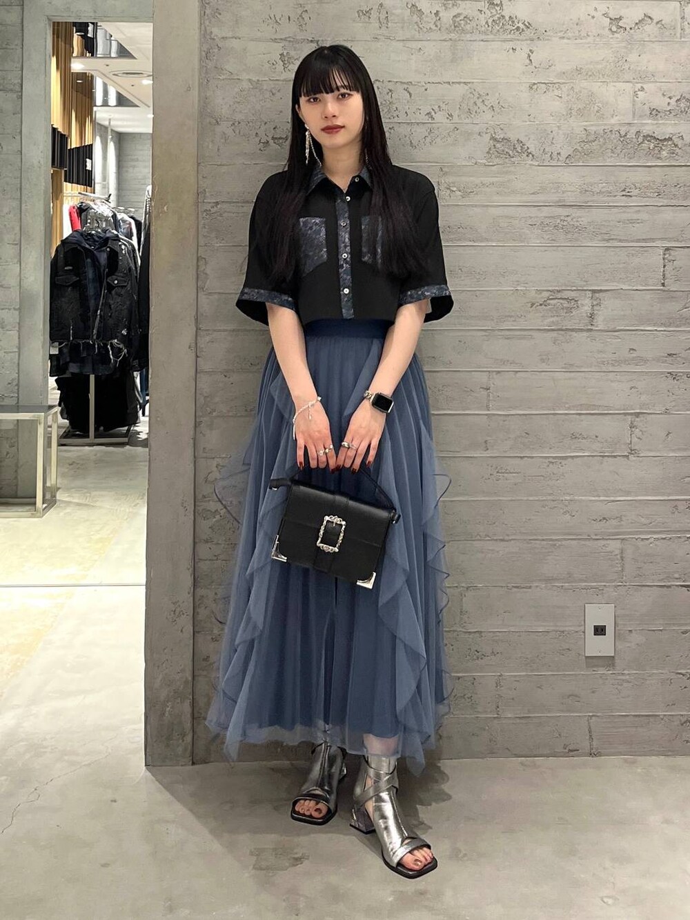 ブラック系のショルダーバッグ、ブルー系のスカート、シルバー系のサンダルを着用したレディースの春コーディネートの1枚目の写真