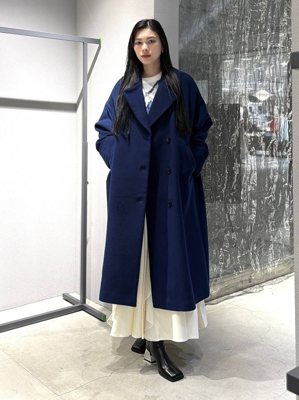 ブルー系のチェスターコート、ブラック系のブーツ、ホワイト系のスカートを着用したレディースの秋コーディネートの1枚目の写真