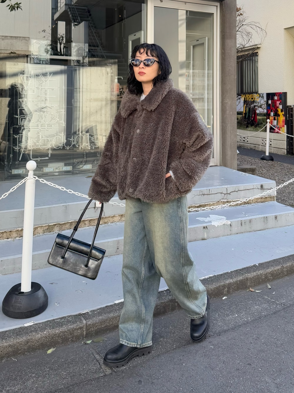 グレー系のムートンコート、グレー系のニット/セーター、ブラック系のハンドバッグを着用したレディースの冬コーディネートの1枚目の写真