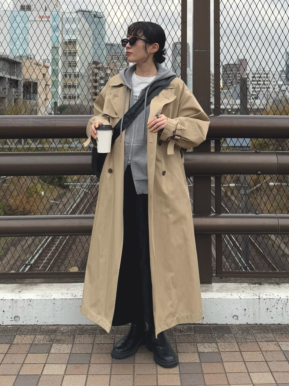 グレー系のパーカー、ベージュ系のトレンチコート、ブラック系のスカートを着用したレディースの冬コーディネートの1枚目の写真