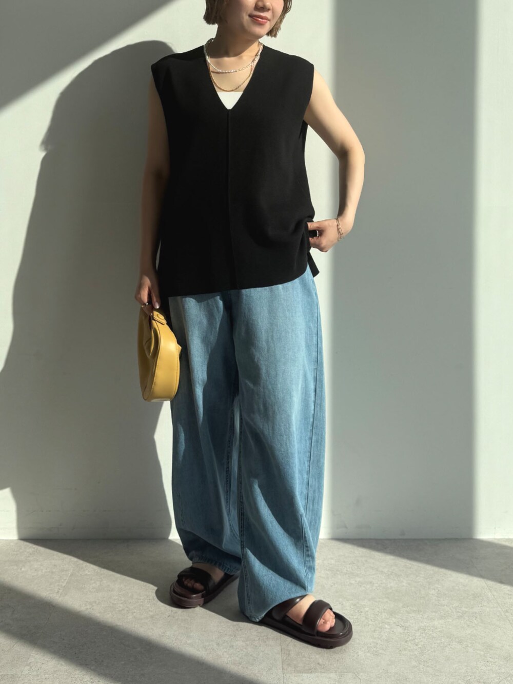 ブルー系のデニムパンツ、ブラック系のベストを着用したレディースの春コーディネートの1枚目の写真