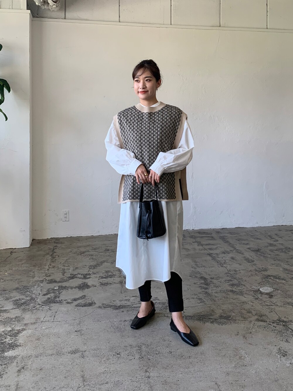 ブラック系のニット/セーター、ホワイト系のシャツワンピース、ブラック系のハンドバッグを着用したレディースの秋コーディネートの1枚目の写真