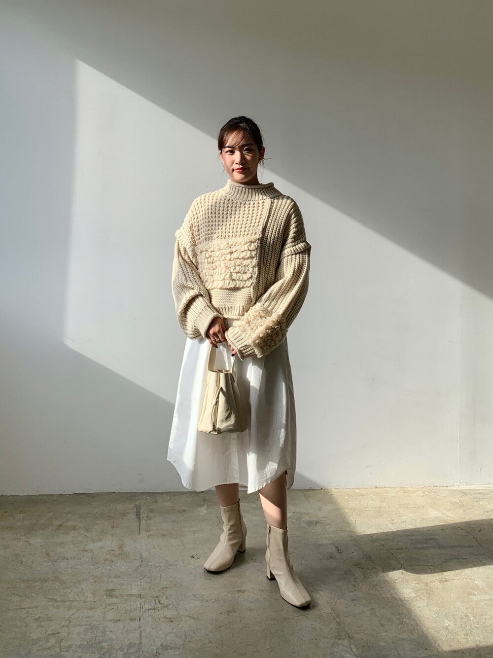 ホワイト系のニット/セーター、ホワイト系のハンドバッグ、ホワイト系のブーツを着用したレディースの秋コーディネートの1枚目の写真