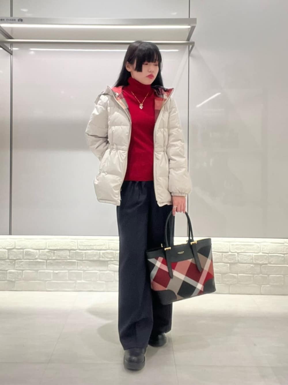 レッド系のハンドバッグ、レッド系のニット/セーター、ベージュ系のダウンジャケット/コートを着用したレディースの秋コーディネートの1枚目の写真