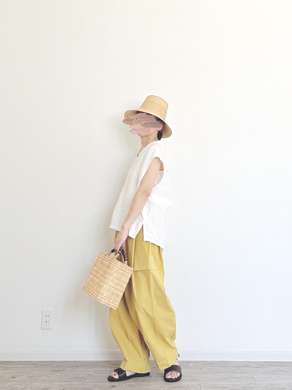 ベージュ系のかごバッグ、イエロー系のカーゴパンツ、ブラウン系のサンダルを着用したレディースの夏コーディネートの1枚目の写真