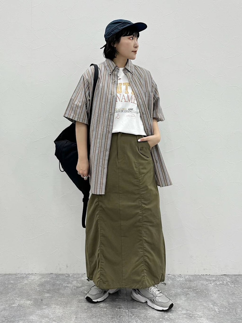 ブラック系のバックパック/リュック、グリーン系のスカート、ホワイト系のTシャツ/カットソーを着用したレディースの春コーディネートの1枚目の写真