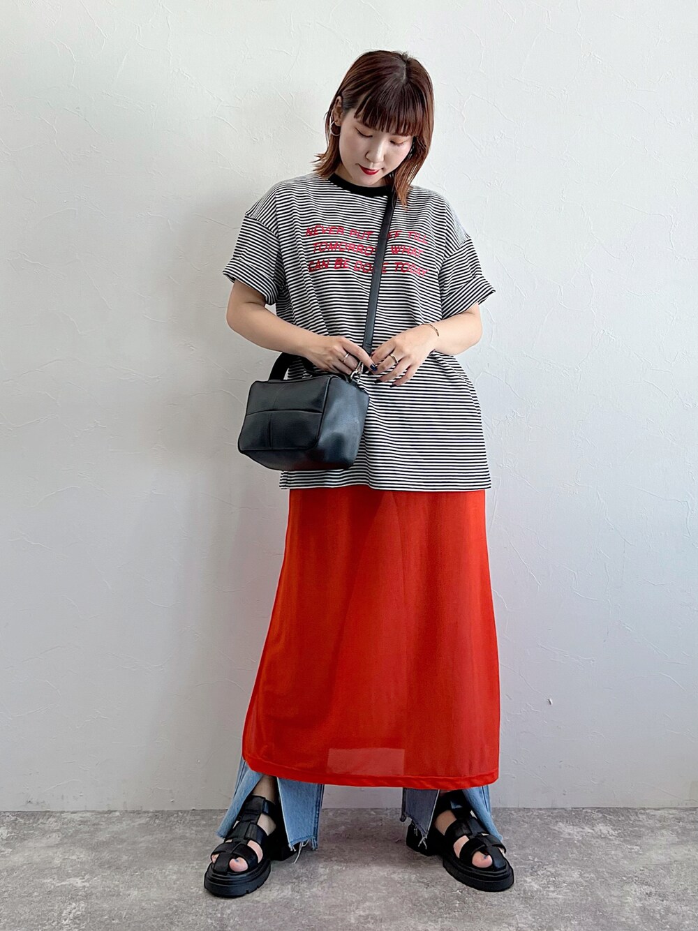 オレンジ系のワンピース、ブラック系のサンダル、ブラック系のTシャツ/カットソーを着用したレディースの夏コーディネートの1枚目の写真