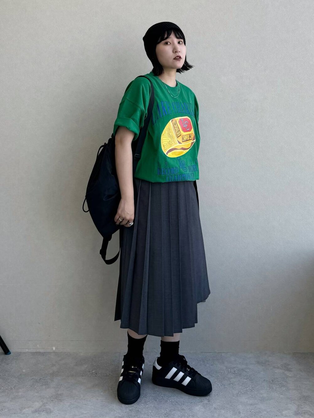 ブラック系のバックパック/リュック、グレー系のスカート、グリーン系のTシャツ/カットソーを着用したレディースの春コーディネートの1枚目の写真