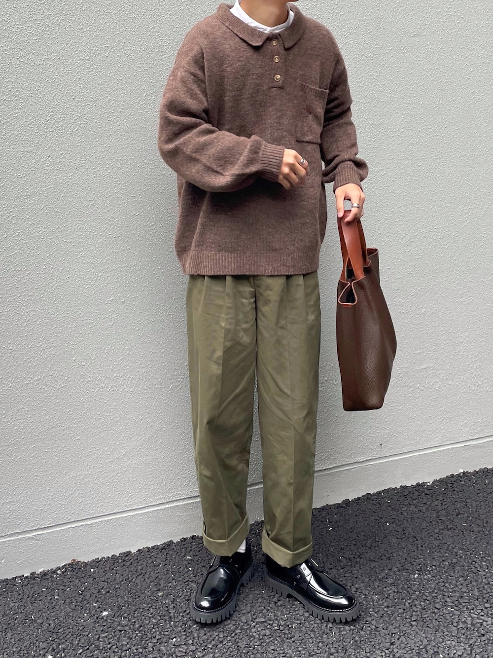 ブラウン系のニット/セーター、グリーン系のチノパンツ、ブラウン系のトートバッグを着用したメンズの秋コーディネートの1枚目の写真
