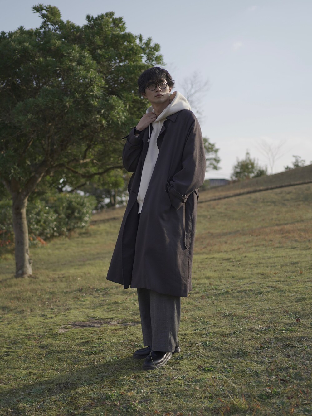 グレー系のトレンチコート、ホワイト系のパーカー、グレー系のスラックスを着用したメンズの冬コーディネートの1枚目の写真