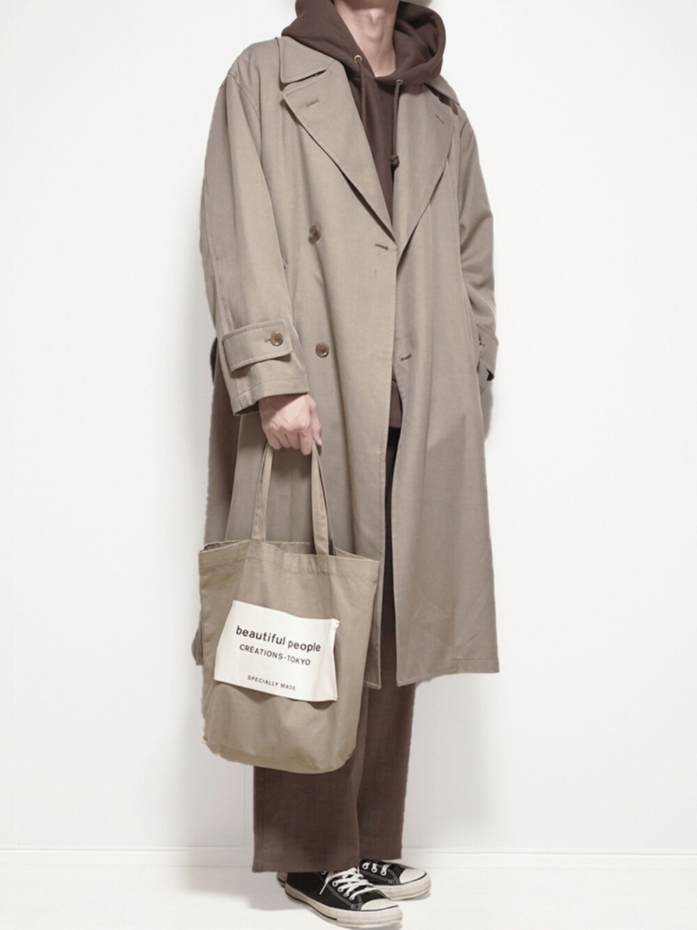 ベージュ系のトレンチコート、ブラウン系のパーカー、ブラウン系のスラックスを着用したメンズの秋コーディネートの1枚目の写真