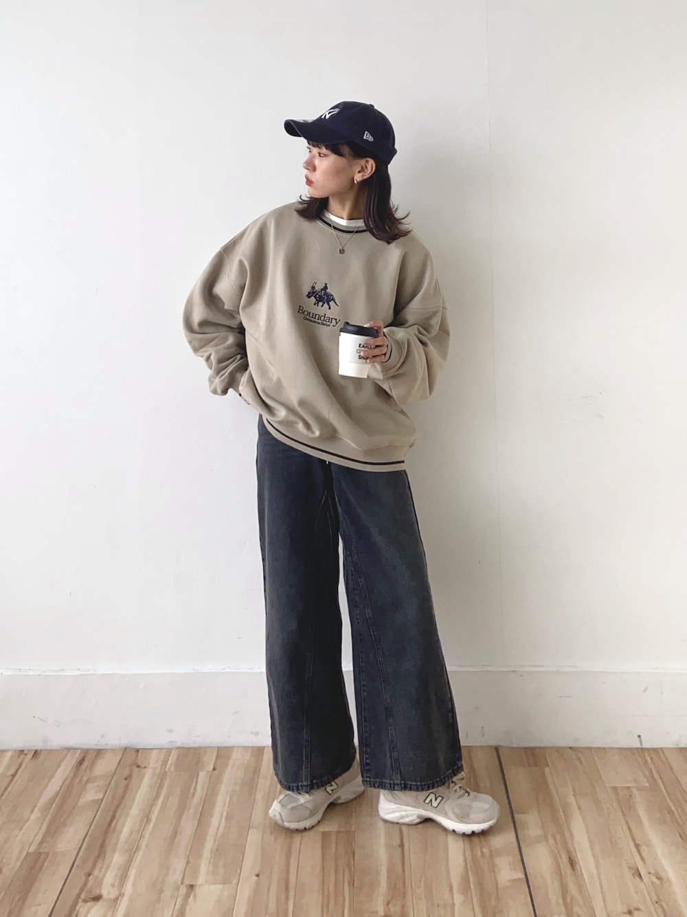 ベージュ系のスウェット、ブラック系のデニムパンツ、ブルー系のキャップを着用したレディースの冬コーディネートの1枚目の写真