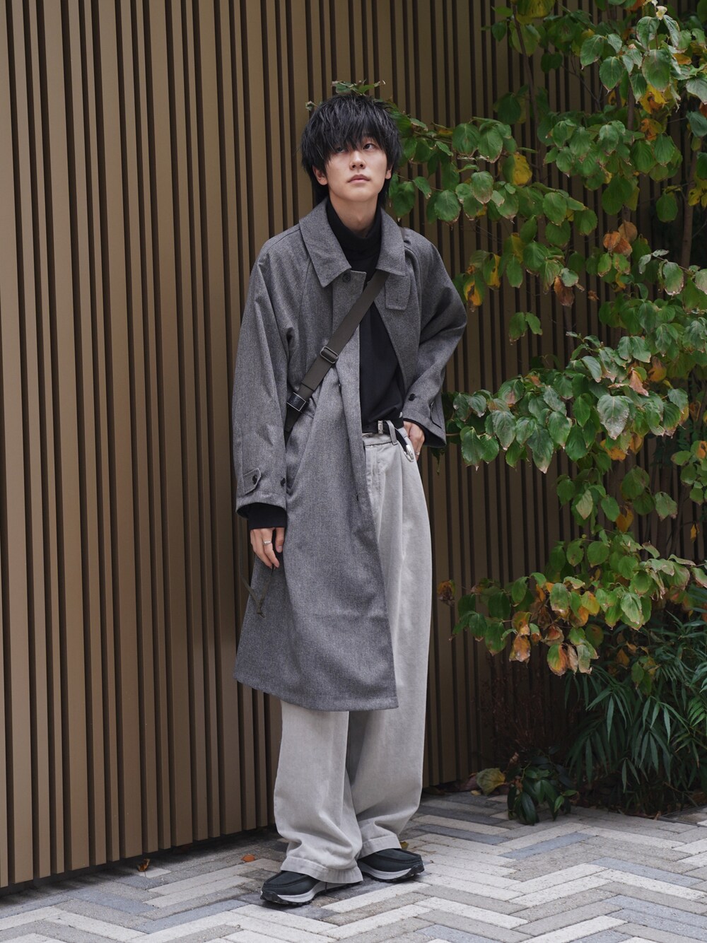 グレー系のステンカラーコート、ブラック系のTシャツ/カットソー、ベージュ系のデニムパンツを着用したメンズの冬コーディネートの1枚目の写真