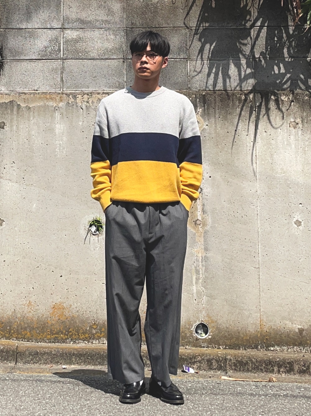 グレー系のスラックス、イエロー系のニット/セーター、ブラック系のローファーを着用したメンズの春コーディネートの1枚目の写真