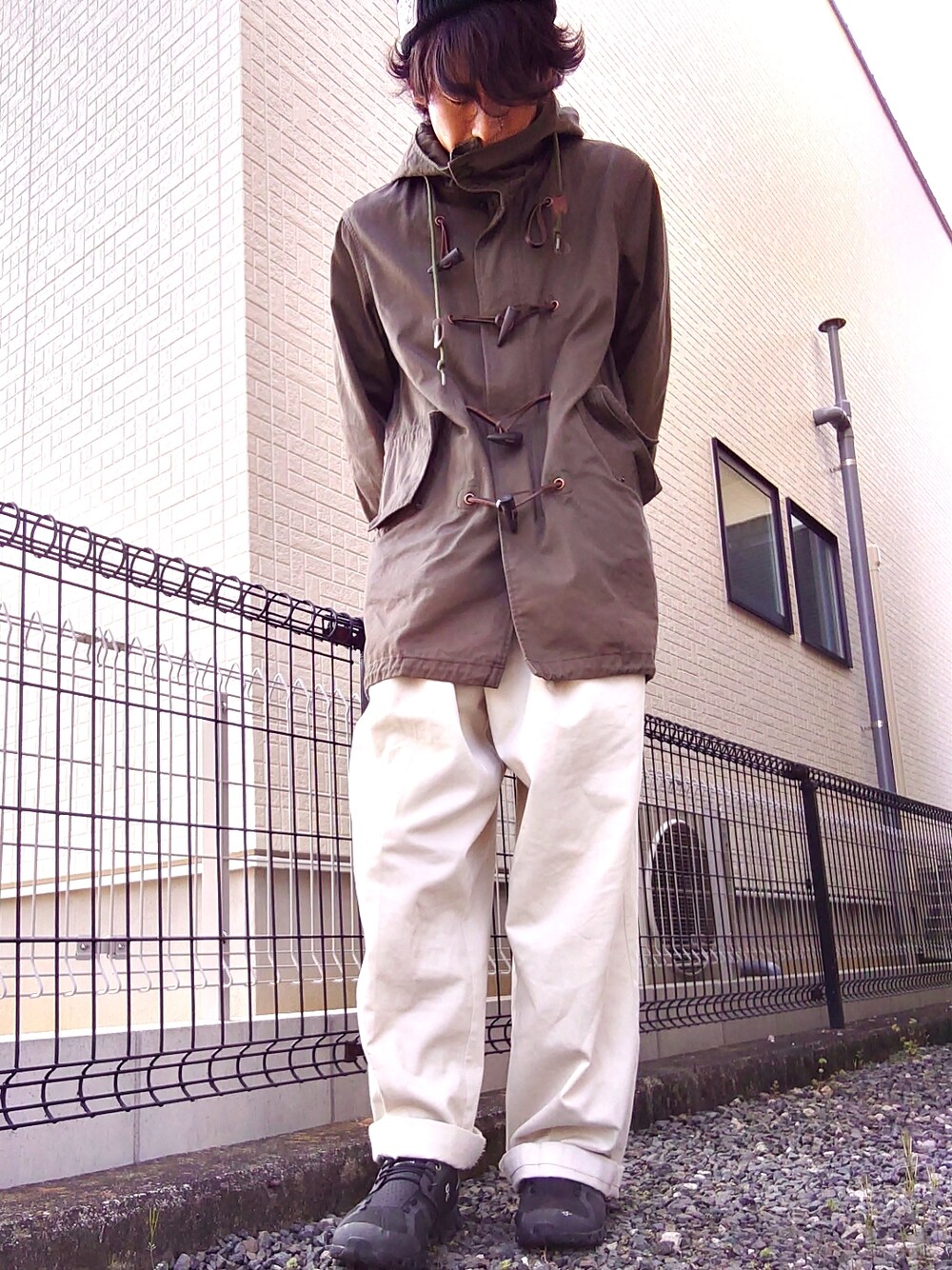 グリーン系のモッズコート、ブラック系のTシャツ/カットソー、ホワイト系のスラックスを着用したメンズの春コーディネートの2枚目の写真