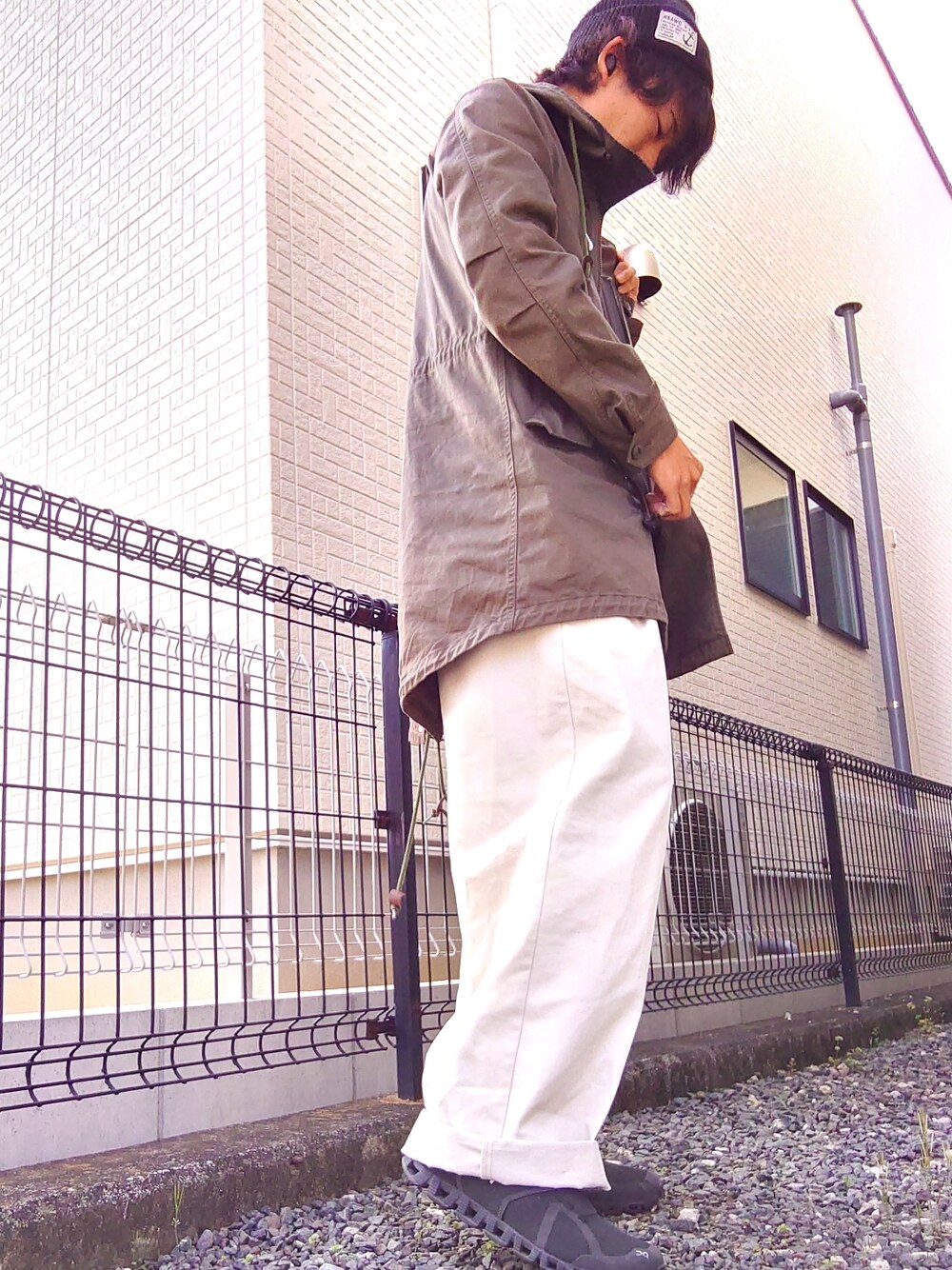 グリーン系のモッズコート、ブラック系のTシャツ/カットソー、ホワイト系のスラックスを着用したメンズの春コーディネートの3枚目の写真