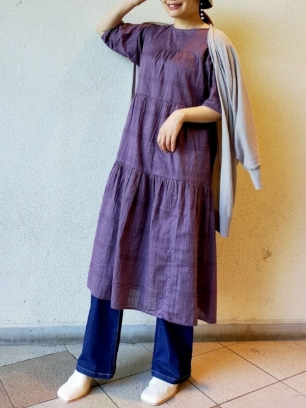 ブルー系のデニムパンツ、パープル系のワンピース、グレー系のカーディガン/ボレロを着用したレディースの秋コーディネートの1枚目の写真