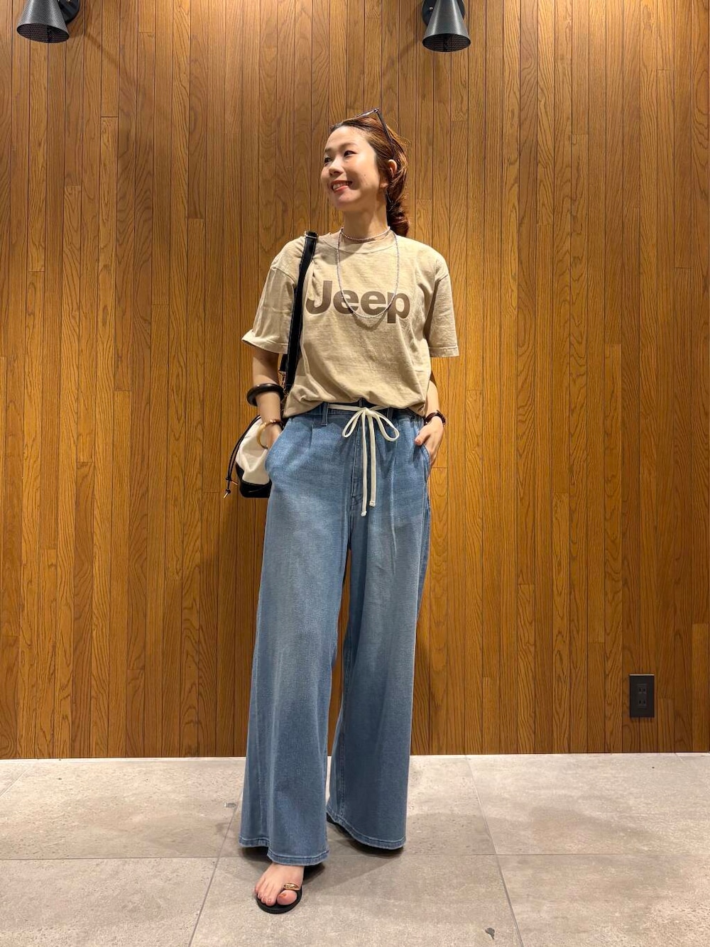 ブルー系のデニムパンツ、ブラック系のサンダル、ベージュ系のTシャツ/カットソーを着用したレディースの夏コーディネートの1枚目の写真