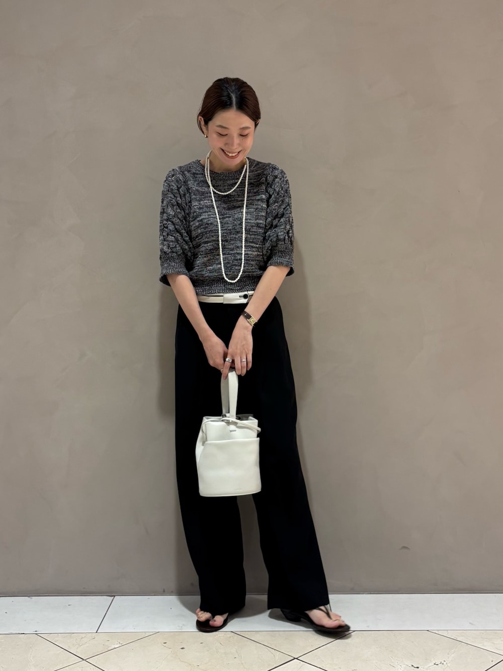 グレー系のニット/セーター、ブラック系のその他パンツ、ホワイト系のハンドバッグを着用したレディースの夏コーディネートの1枚目の写真