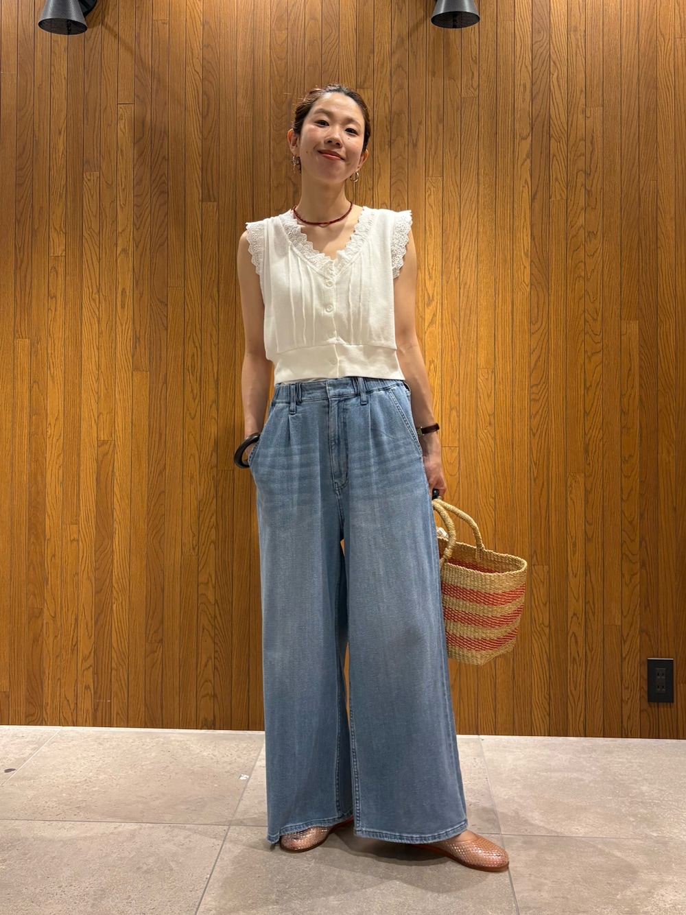 ブルー系のデニムパンツ、ホワイト系のベスト、ベージュ系のかごバッグを着用したレディースの夏コーディネートの1枚目の写真