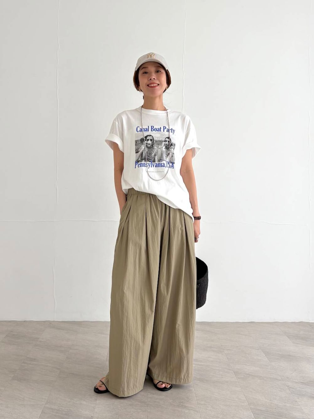 ベージュ系のその他パンツ、ブラック系のかごバッグ、ブラック系のサンダルを着用したレディースの夏コーディネートの1枚目の写真