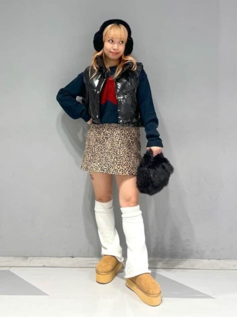 ブルー系のニット/セーター、ブラック系のダウンベスト、ブラウン系のスカートを着用したレディースの秋コーディネートの1枚目の写真