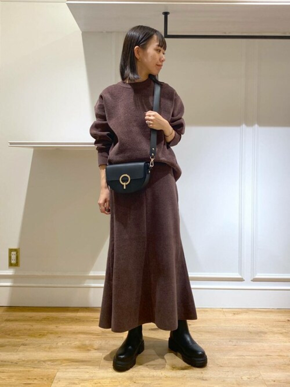 ブラウン系のニット/セーター、ブラウン系のスカート、ブラック系のブーツを着用したレディースの秋コーディネートの1枚目の写真