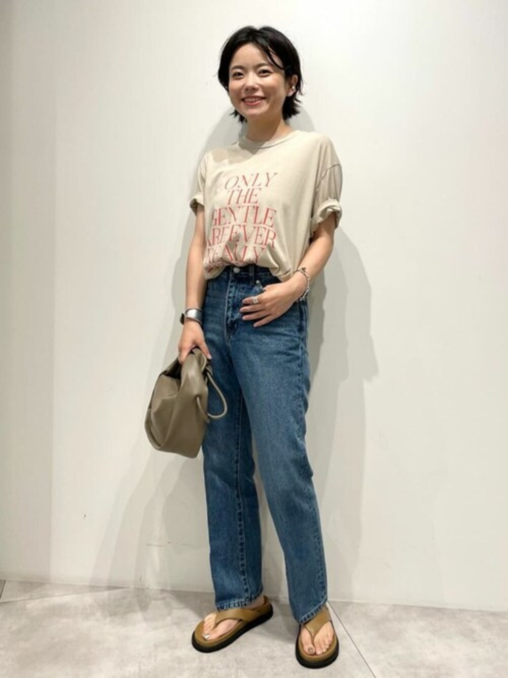 ブルー系のデニムパンツ、ベージュ系のTシャツ/カットソー、ブラウン系のショルダーバッグを着用したレディースの秋コーディネートの1枚目の写真