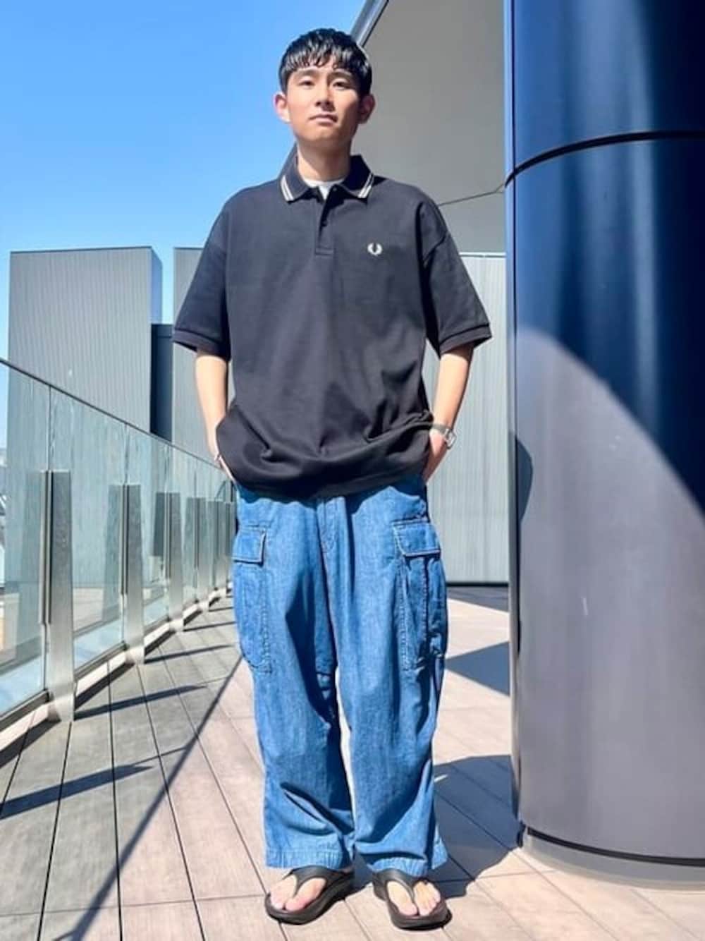 ブラック系のポロシャツ、ブルー系のカーゴパンツを着用したメンズの春コーディネートの1枚目の写真