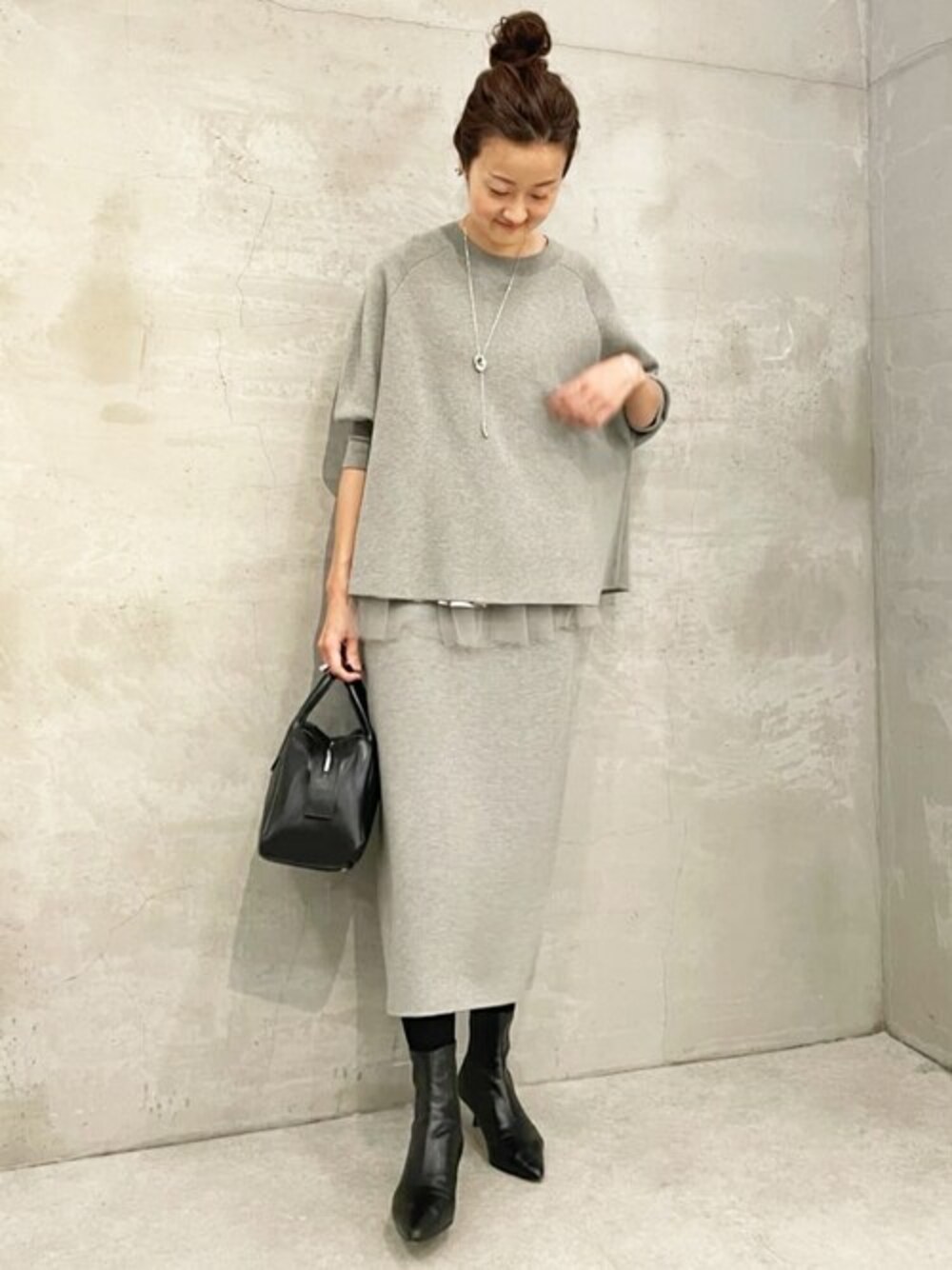 グレー系のニット/セーター、ブラック系のショルダーバッグ、ブラック系のブーツを着用したレディースの秋コーディネートの1枚目の写真