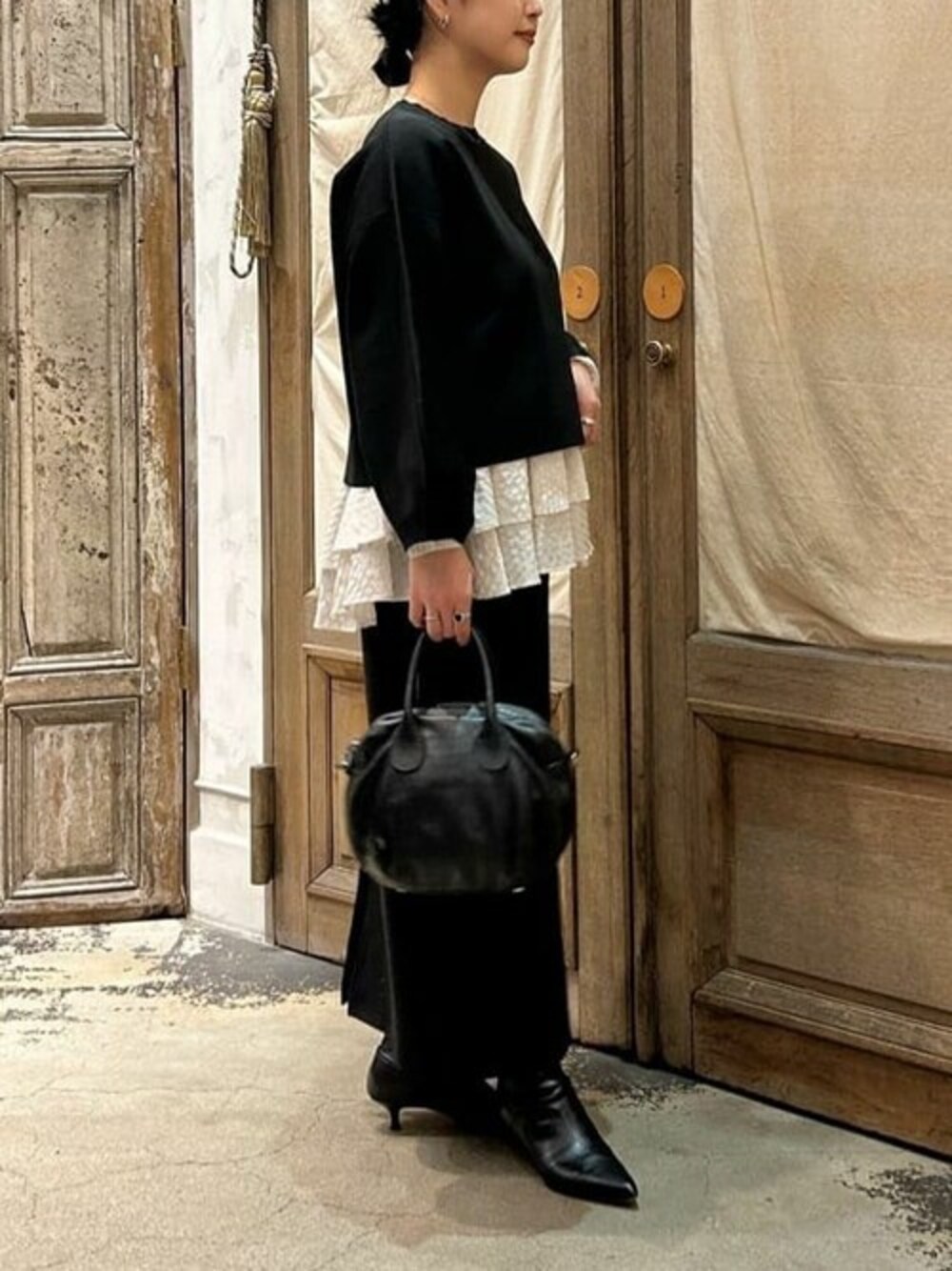 ブラック系のショルダーバッグ、ブラック系のニット/セーター、ホワイト系のシャツ/ブラウスを着用したレディースの冬コーディネートの1枚目の写真