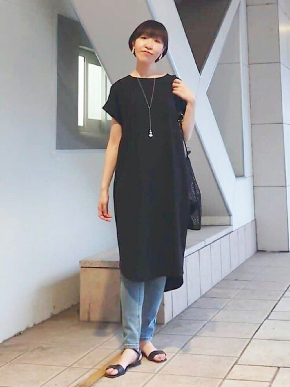 ブラック系のワンピース、ブルー系のデニムパンツ、ブラック系のショルダーバッグを着用したレディースの春コーディネートの1枚目の写真