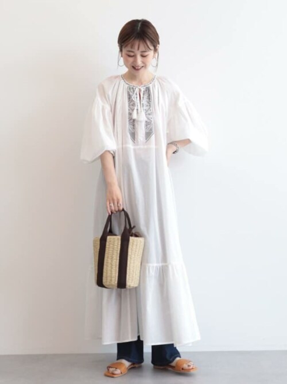 ホワイト系のワンピース、ブルー系のデニムパンツ、ベージュ系のハンドバッグを着用したレディースの春コーディネートの1枚目の写真