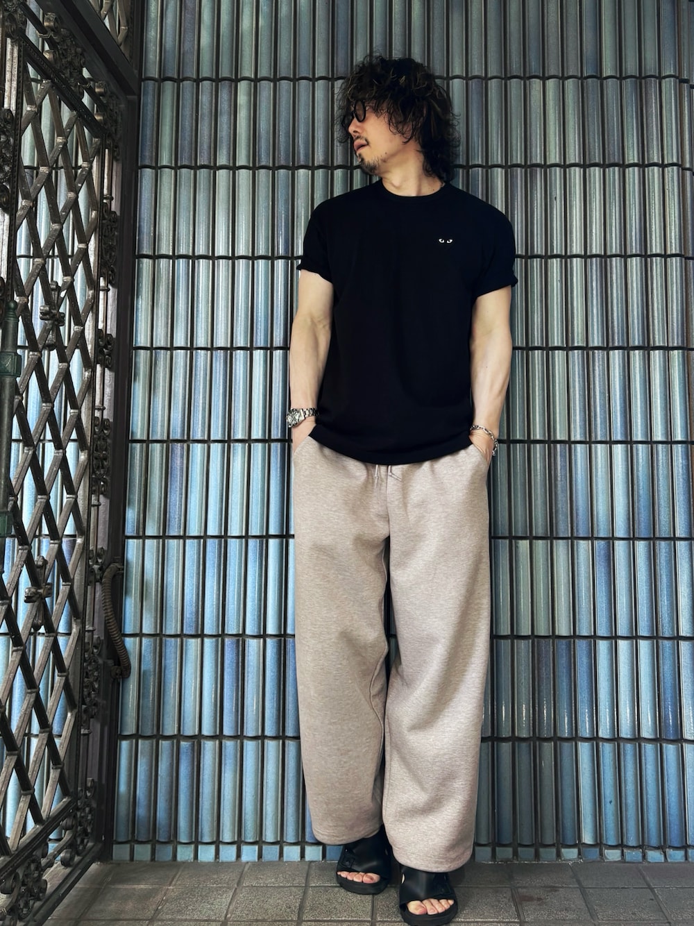 ブラック系のサンダル、ブラック系のTシャツ/カットソー、ベージュ系のスウェットパンツを着用したメンズの夏コーディネートの1枚目の写真