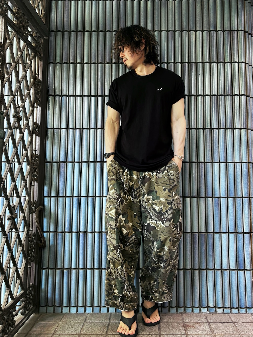 グリーン系のカーゴパンツ、ブラック系のサンダル、ブラック系のTシャツ/カットソーを着用したメンズの夏コーディネートの1枚目の写真