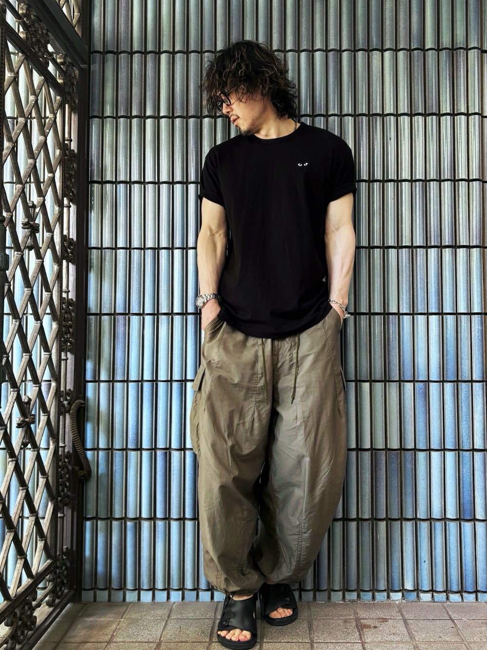グリーン系のカーゴパンツ、ブラック系のサンダル、ブラック系のTシャツ/カットソーを着用したメンズの夏コーディネートの1枚目の写真