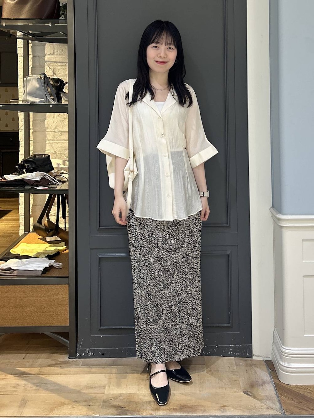 ホワイト系のショルダーバッグ、ベージュ系のスカート、ブラック系のパンプスを着用したレディースの夏コーディネートの1枚目の写真