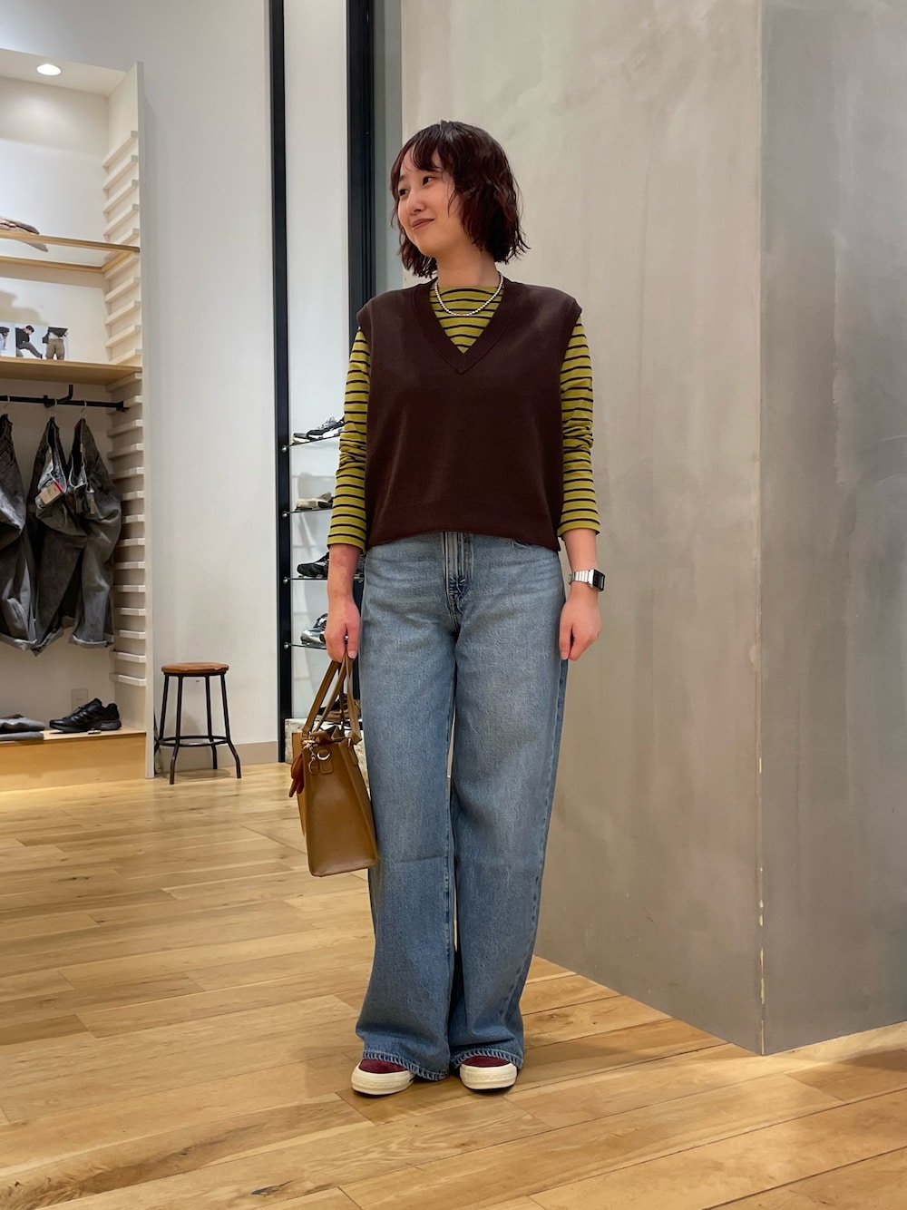 ブルー系のデニムパンツ、ブラウン系のベスト、イエロー系のTシャツ/カットソーを着用したレディースの秋コーディネートの1枚目の写真
