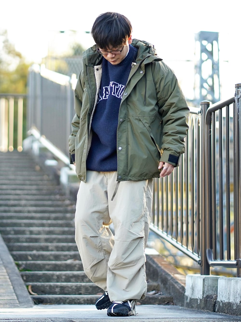 グリーン系のマウンテンパーカー、ブルー系のニット/セーター、グレー系のその他パンツを着用したメンズの冬コーディネートの1枚目の写真