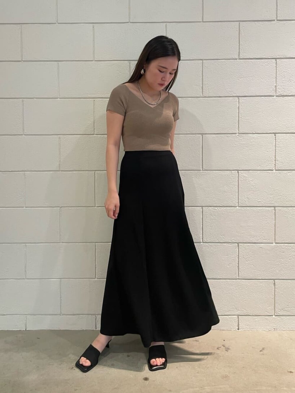 ベージュ系のニット/セーター、ブラック系のスカート、ブラック系のサンダルを着用したレディースの夏コーディネートの1枚目の写真