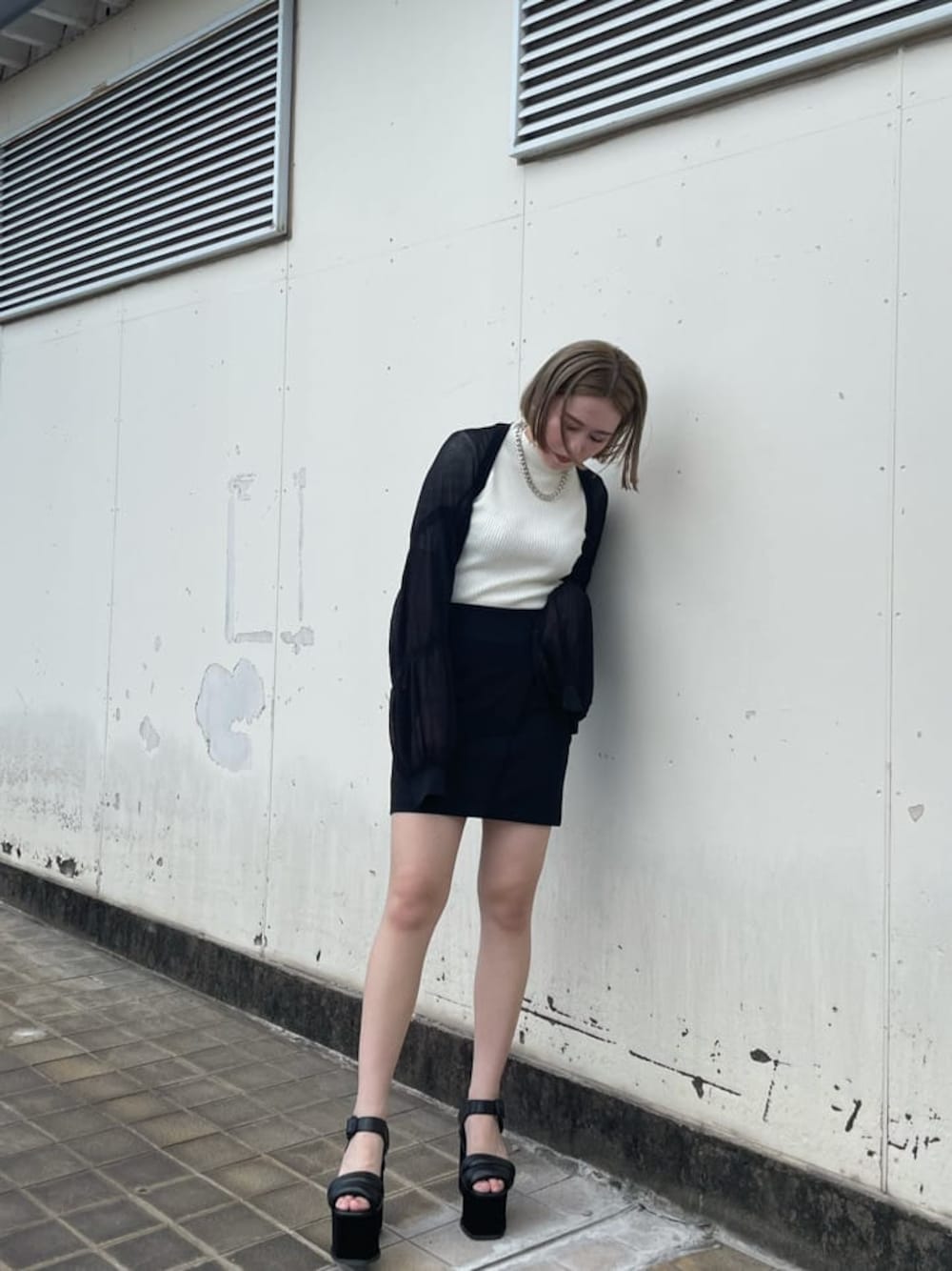 ブラック系のスカート、ブラック系のサンダル、ホワイト系のニット/セーターを着用したレディースの秋コーディネートの1枚目の写真