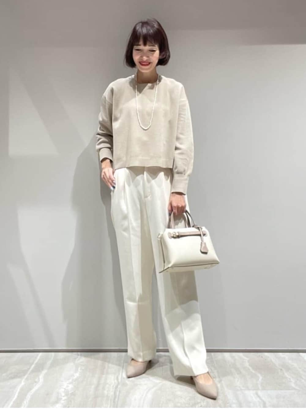 ベージュ系のニット/セーター、ホワイト系のスラックス、ゴールド系のネックレスを着用したレディースの秋コーディネートの1枚目の写真