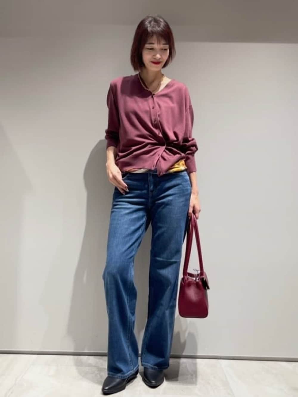 ブルー系のデニムパンツ、レッド系のカーディガン/ボレロ、ゴールド系のネックレスを着用したレディースの秋コーディネートの1枚目の写真