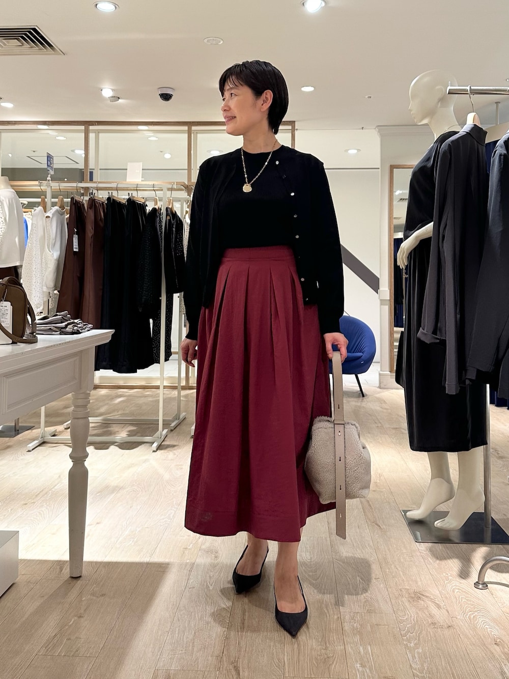 レッド系のスカート、ベージュ系のショルダーバッグ、ブラック系のニット/セーターを着用したレディースの秋コーディネートの1枚目の写真